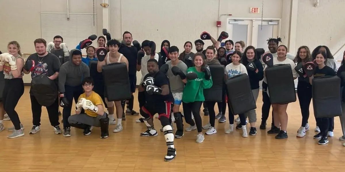 Instructor MJ with a full kickboxing class holding pads and gloves
